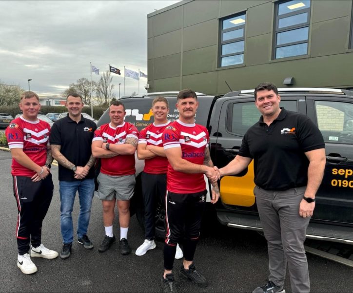 Group of men posing in sports jerseys alongside a branded vehicle, with two in black shirts shaking hands.